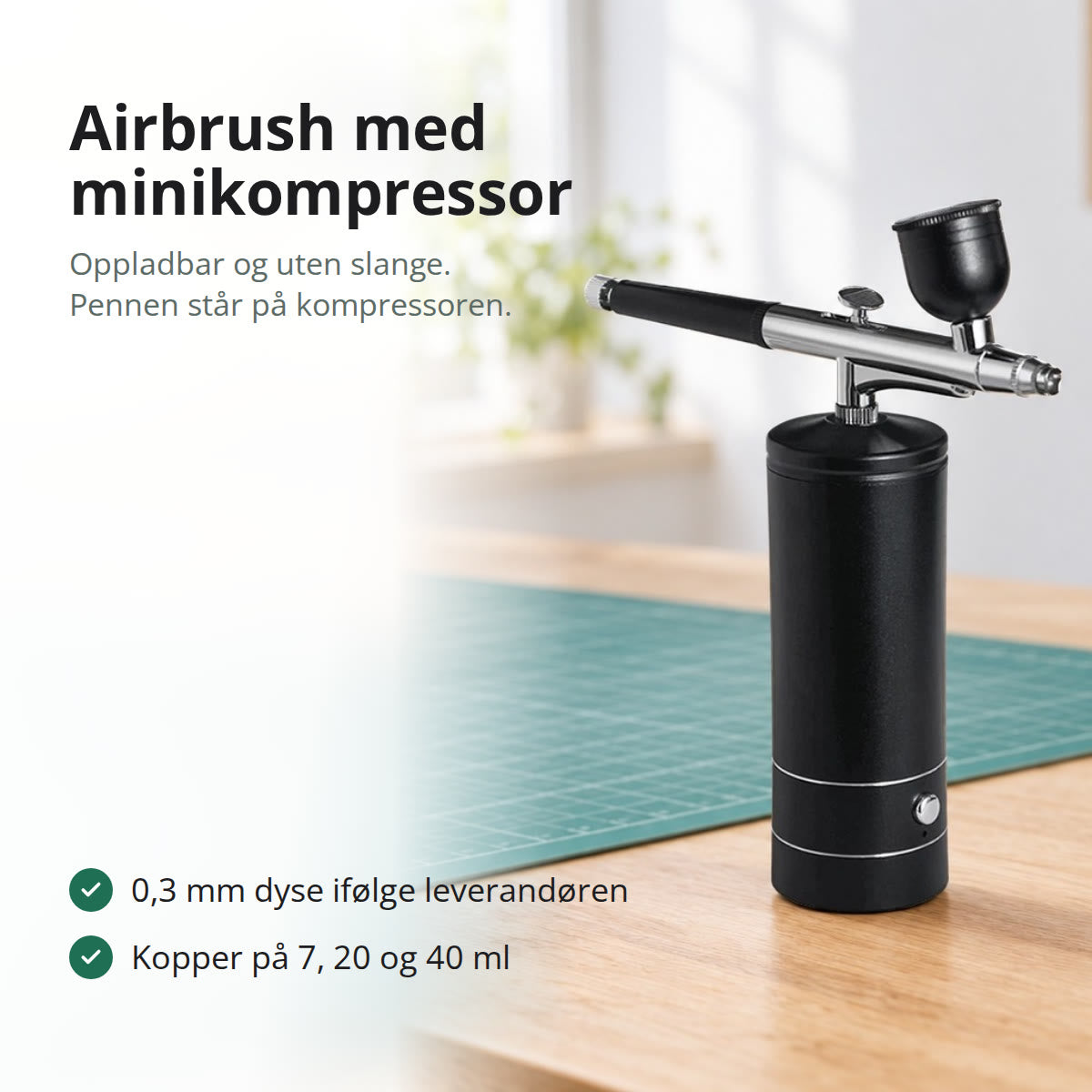 Svart airbrush-penn montert på en oppladbar minikompressor, stående på en lys arbeidsbenk i eik