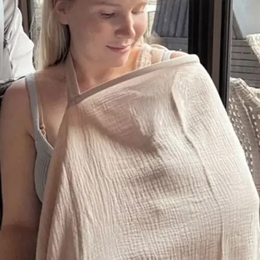 Kvinne med kakifarget ammesjal over skuldrene som ser ned på babyen