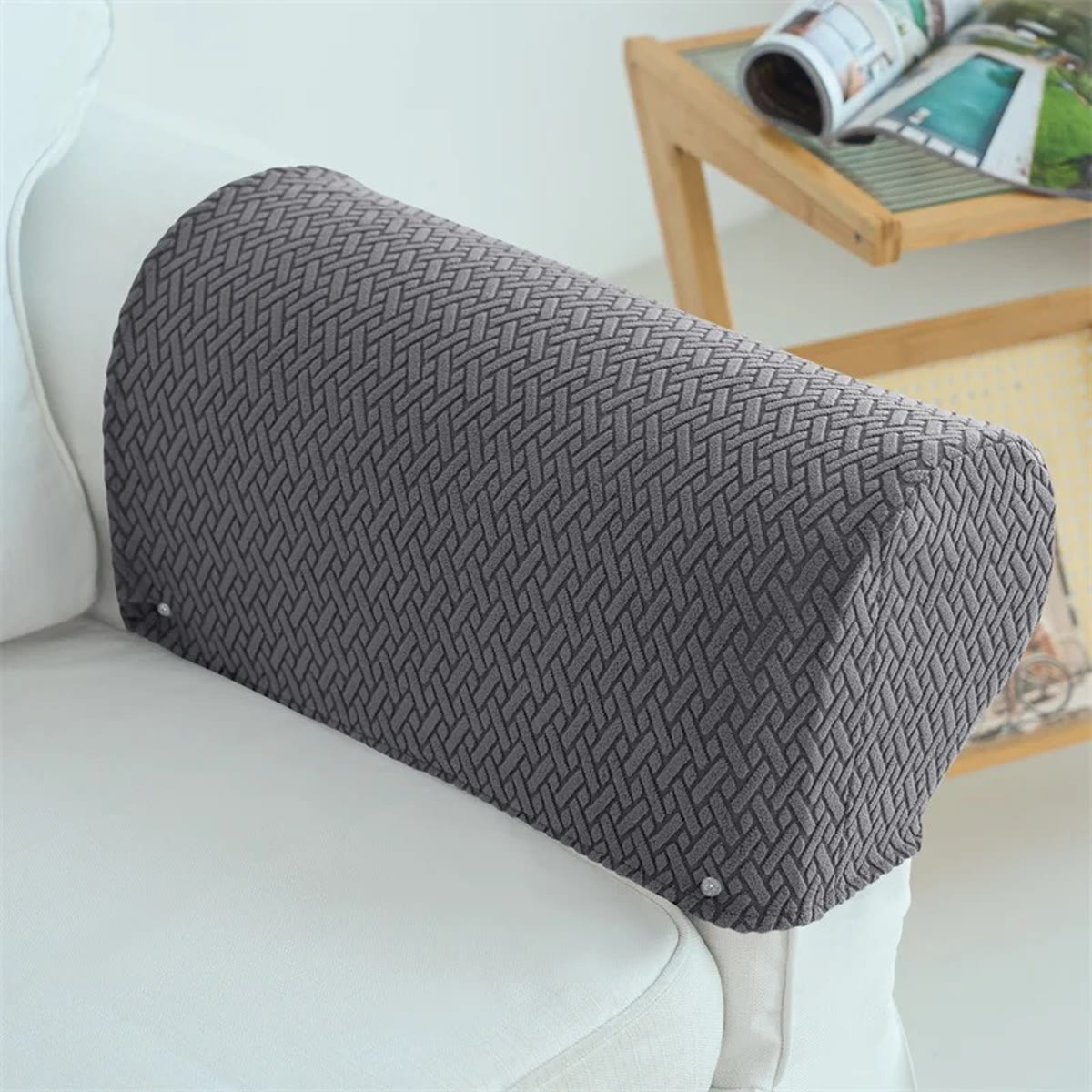 Grått armlenetrekk i vevd jacquard tredd over armlenet på en hvit sofa, med et sidebord i lyst tre bak