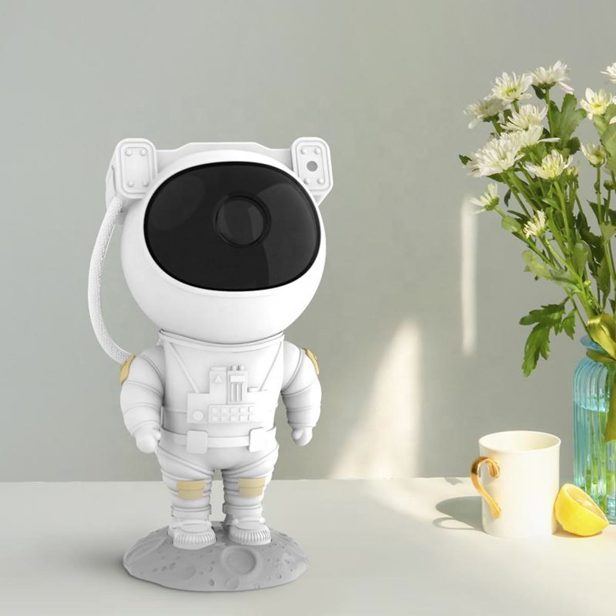 Hvit astronaut-projektor på et bord ved et vindu, med en vase med blomster bak