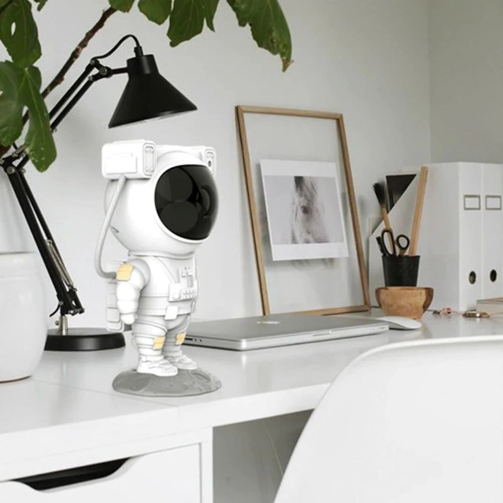 Astronaut-projektoren på et skrivebord ved siden av en laptop og en lampe