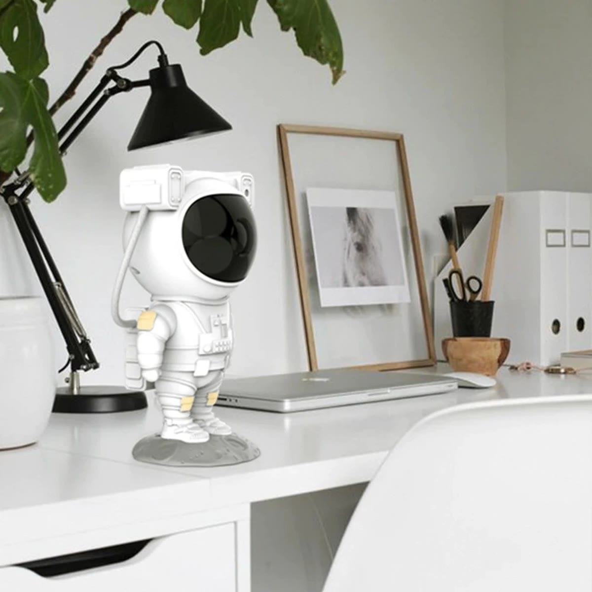 Astronaut-projektoren på et skrivebord ved siden av en laptop og en lampe