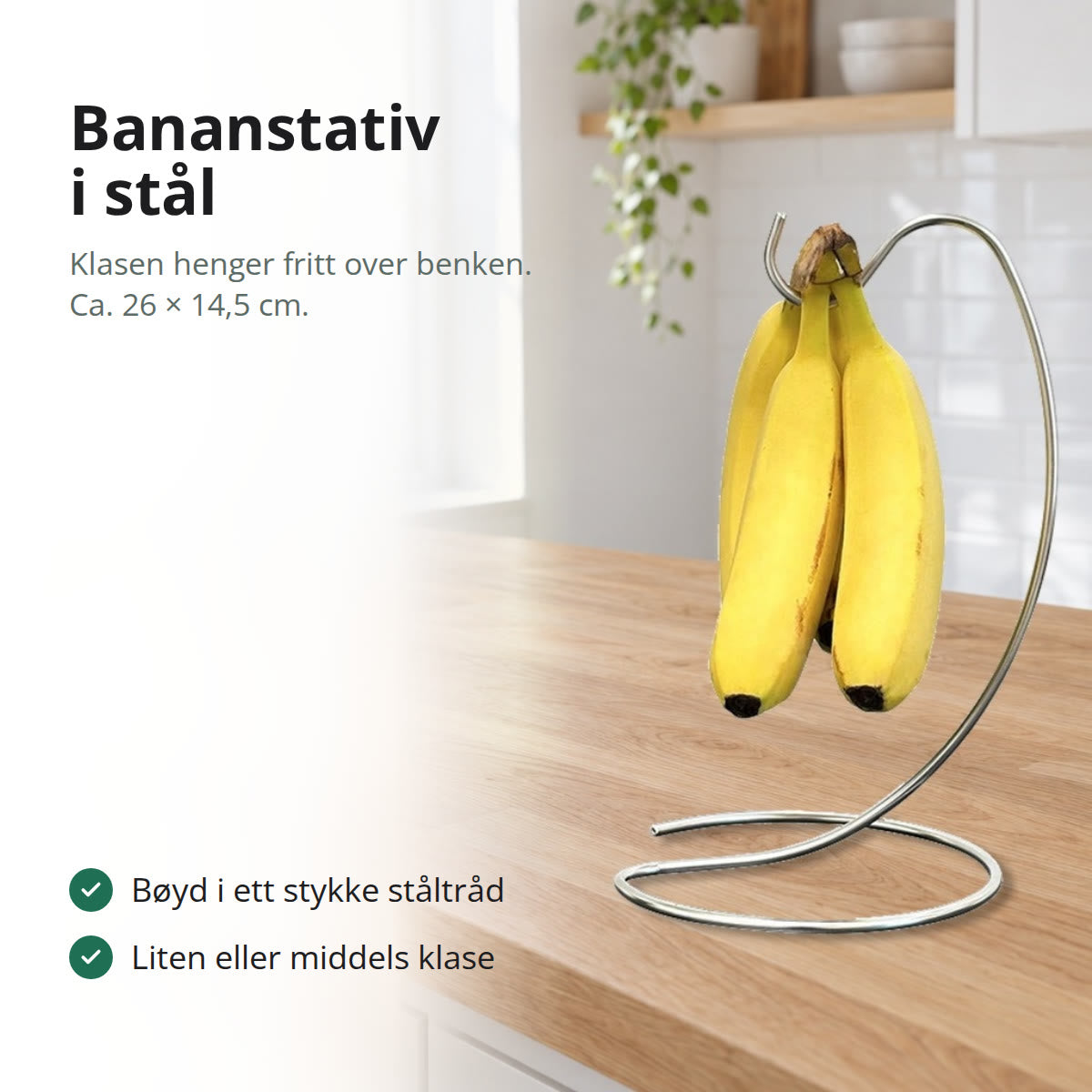 Bananstativ i sølvfarget ståltråd med en liten klase bananer på kroken, på en kjøkkenbenk i lys eik