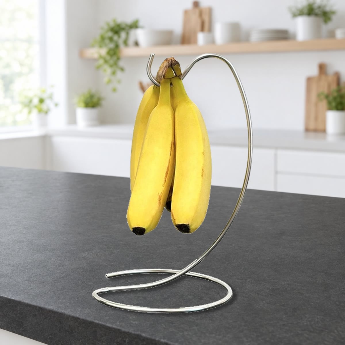 Bananstativet med en liten klase på kroken, stående på en mørk benkeplate i et lyst kjøkken