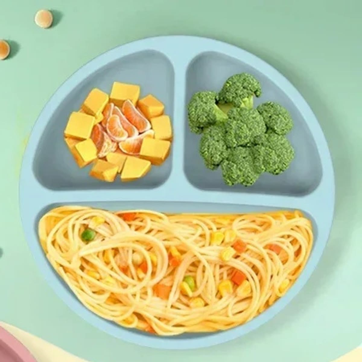 Blå tallerken i silikon med tre rom, fylt med pasta, brokkoli og frukt