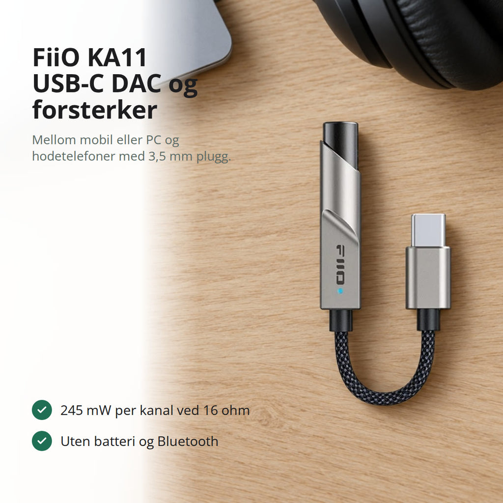 Titanfarget KA11 USB-C DAC og forsterker liggende på et lyst eikeskrivebord, ved siden av en bærbar PC og svarte hodetelefoner