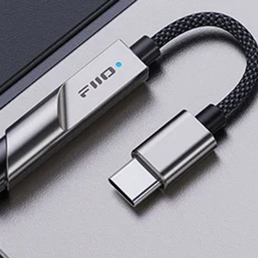 KA11 i titanfarge på en grå flate, med 3,5 mm-utgangen, kabinettet med lys, den flettede kabelen og USB-C-pluggen
