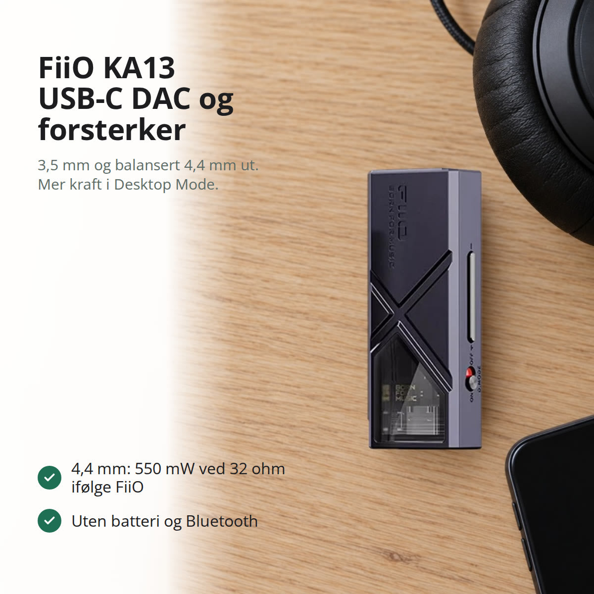 Svart KA13 USB-C DAC og hodetelefonforsterker på et lyst eikeskrivebord, ved siden av hodetelefoner med kabel og en mobil