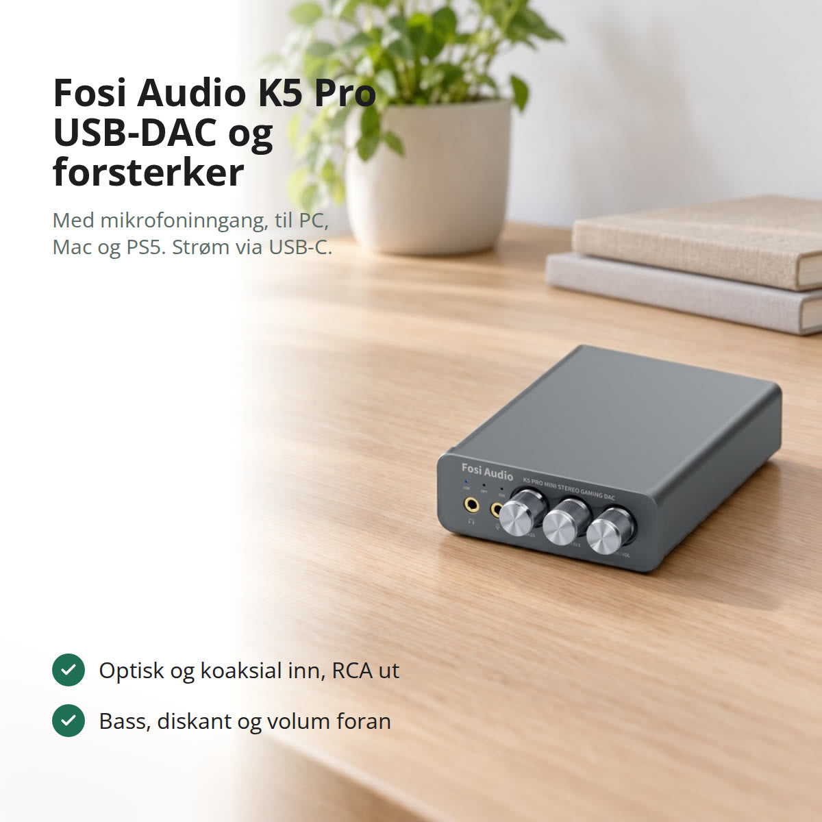 Grå K5 Pro USB-DAC og hodetelefonforsterker på et lyst eikeskrivebord ved et vindu med utsikt mot en fjord
