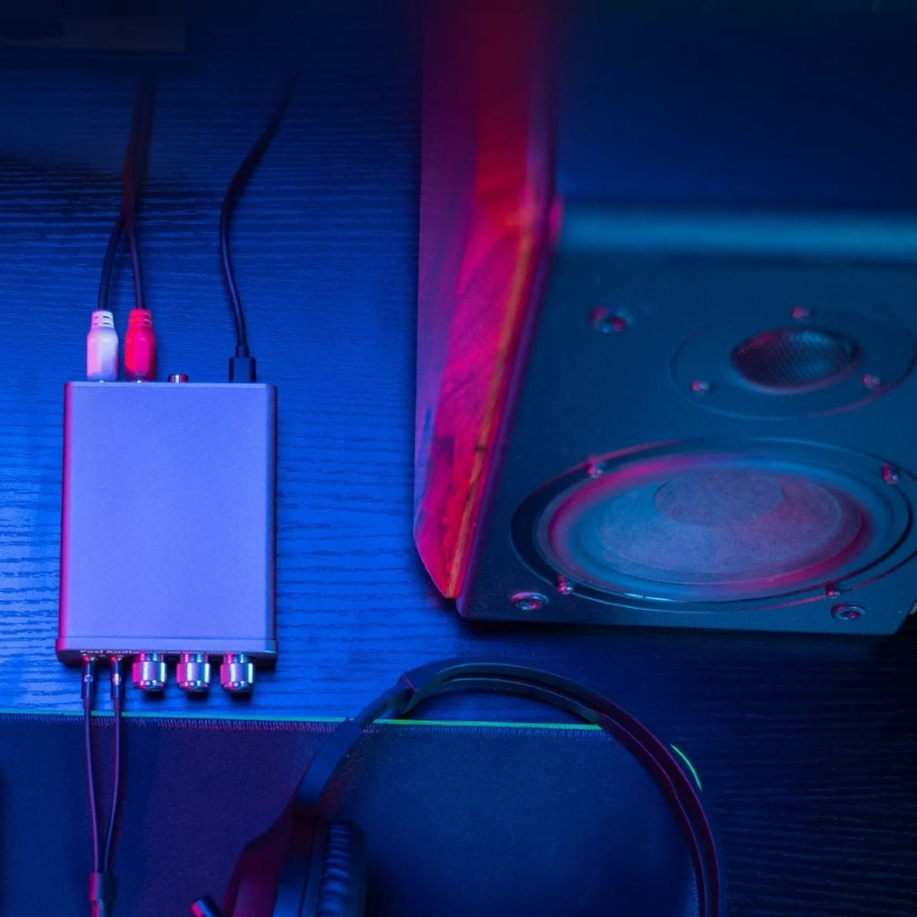 K5 Pro sett ovenfra med RCA-kabler og USB-C-kabel bak og plugger for headset foran, ved siden av en aktiv høyttaler