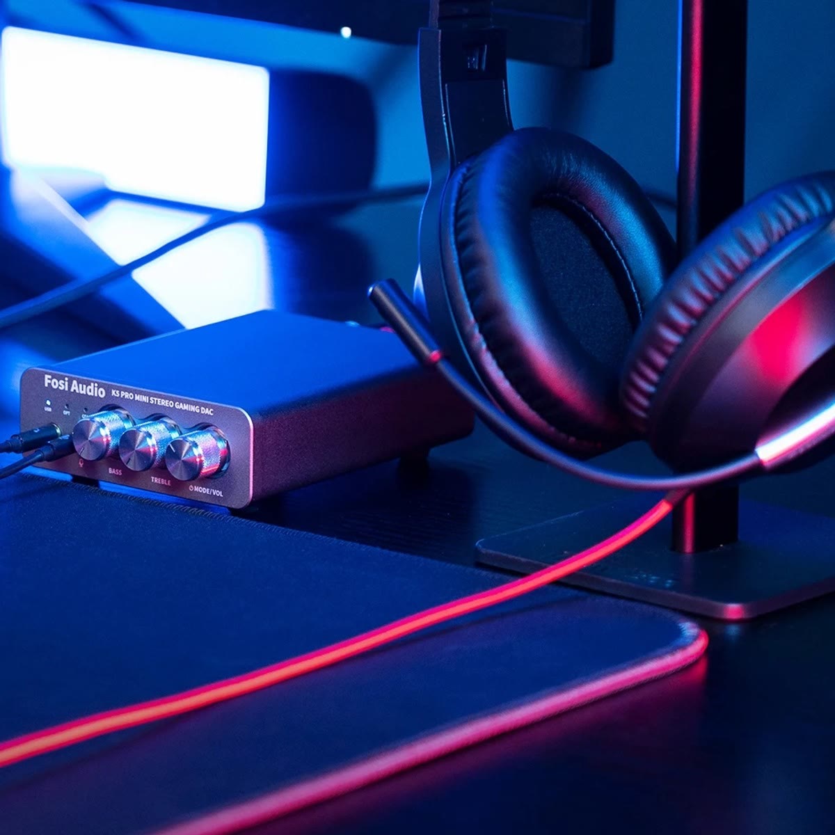 K5 Pro på et gamingskrivebord med plugger i hodetelefon- og mikrofonuttaket, ved siden av et headset på et stativ