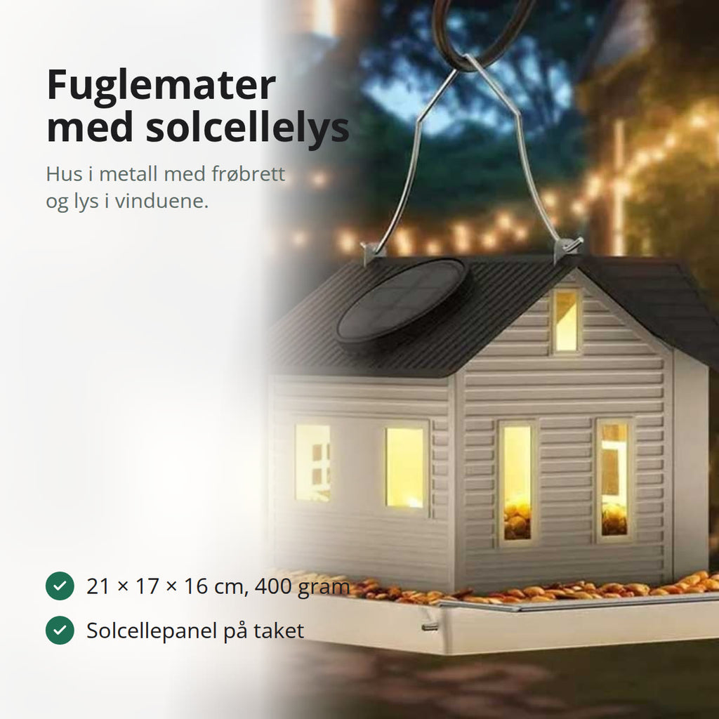 Fuglemater formet som et hvitt hus i metall med sort tak, solcellepanel og brett for frø