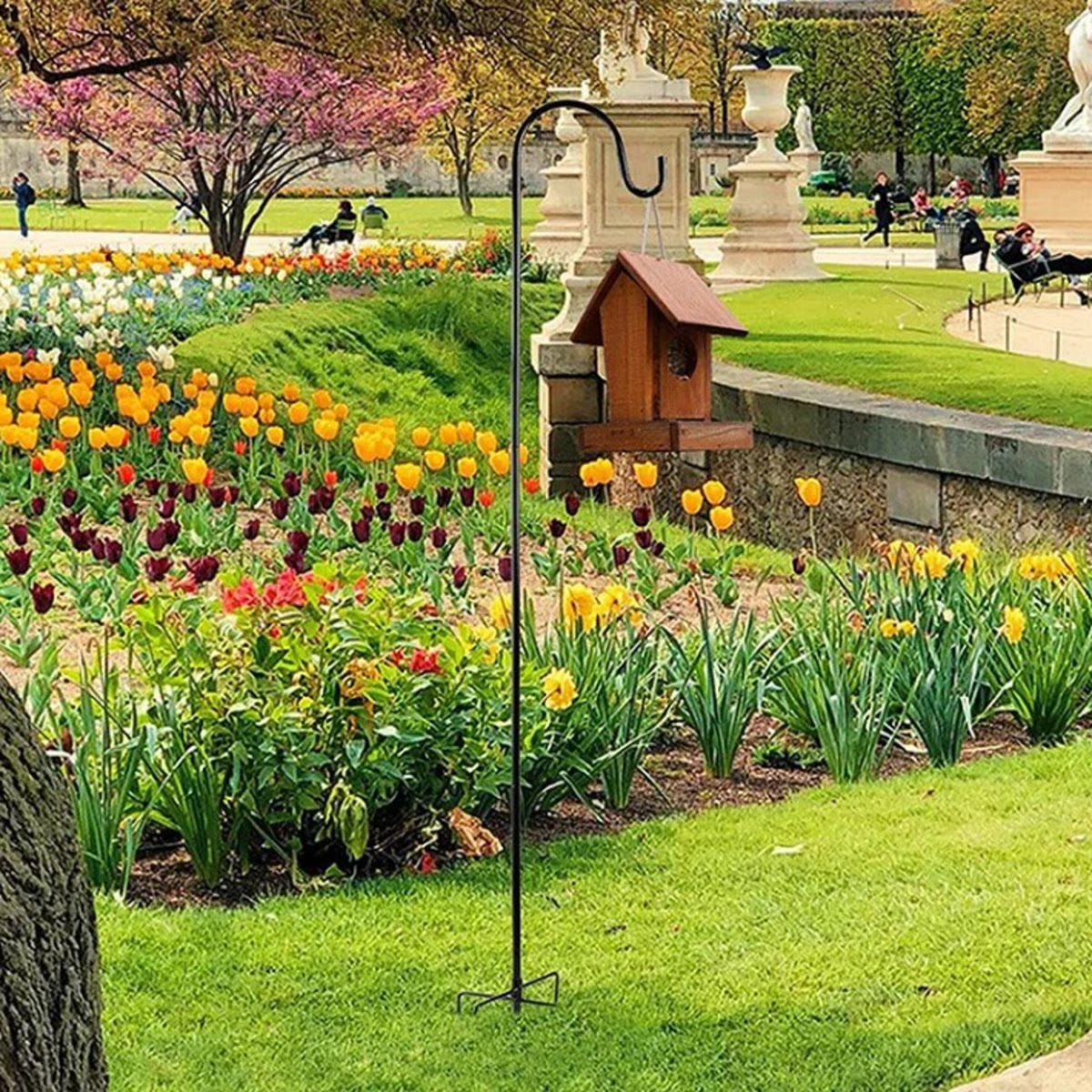 Svart krok stukket ned i et blomsterbed med tulipaner, med et lite fuglehus i tre hengende i kroken