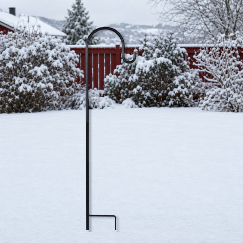 Svart krok i metall med fotbøyle stukket ned i snøen i en hage om vinteren