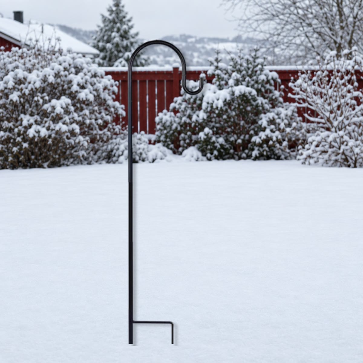 Svart krok i metall med fotbøyle stukket ned i snøen i en hage om vinteren