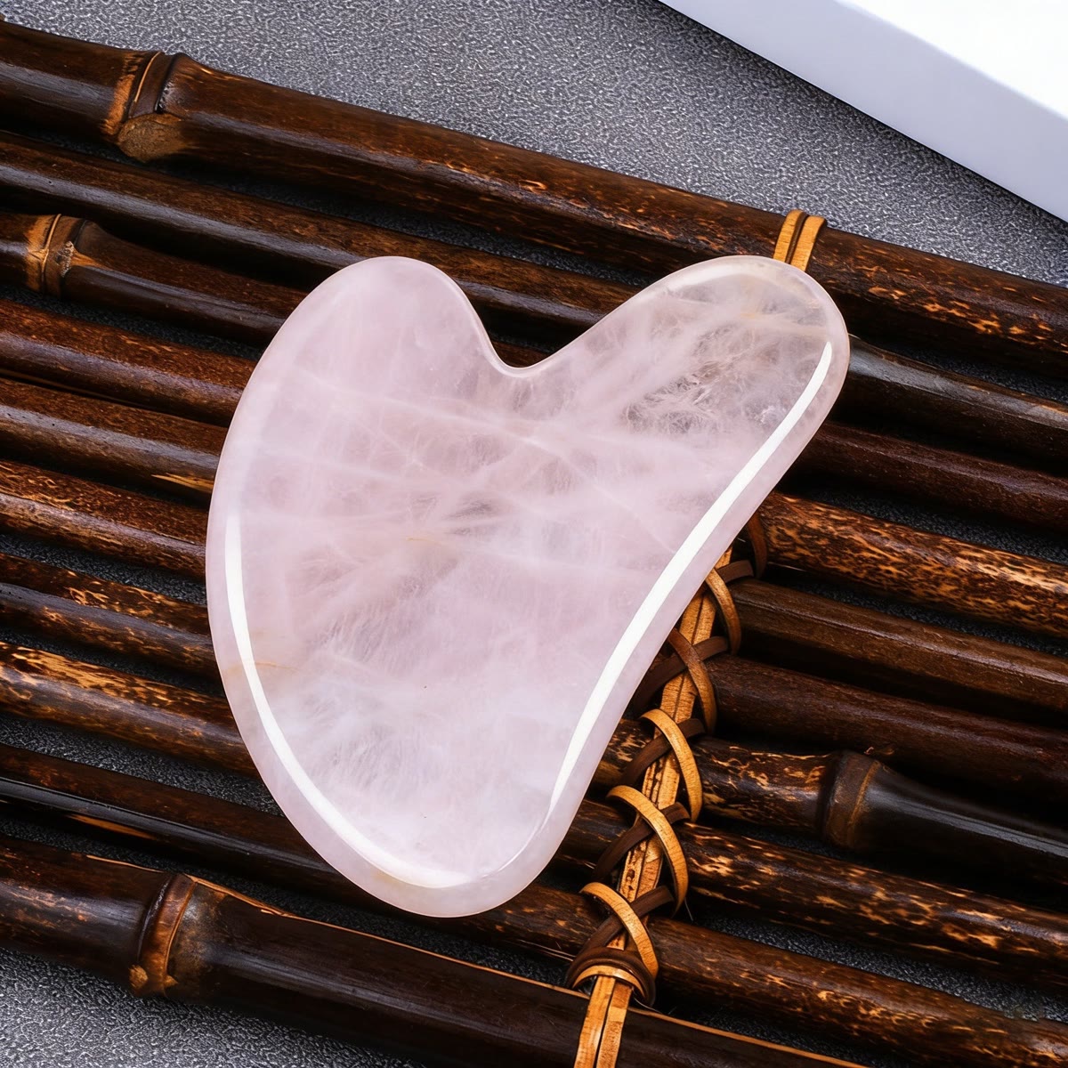 Gua sha i rosenkvarts som ligger på en matte av bambuspinner