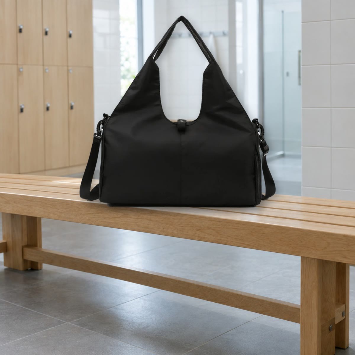 Svart gymbag med bærehåndtak og skulderstropp på en trebenk i en garderobe