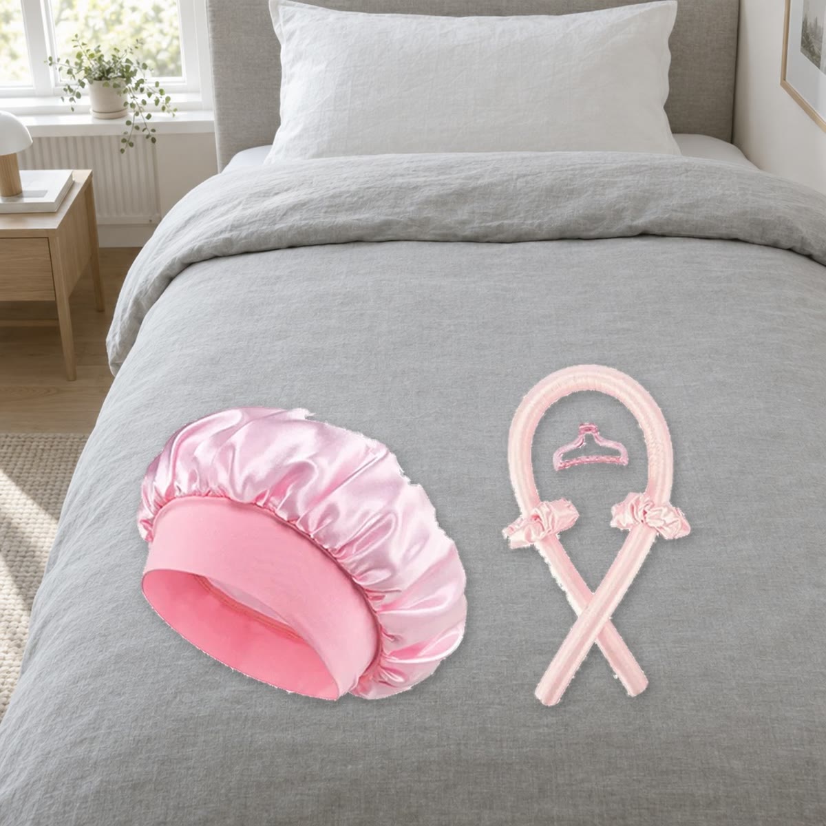 Heatless curls-sett i rosa: krøllestav, satenghette, to scrunchies og hårklype på en grå sengetøy