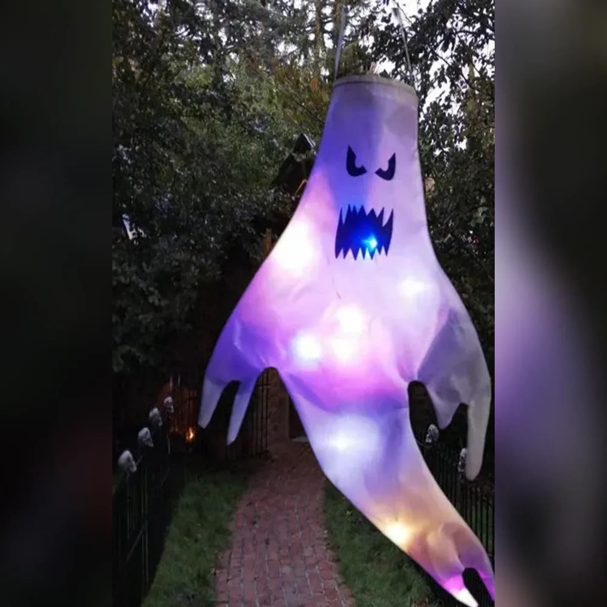 Tent halloween spøkelse med sint ansikt og lilla og hvite LED-lys, hengende over en hagesti om kvelden
