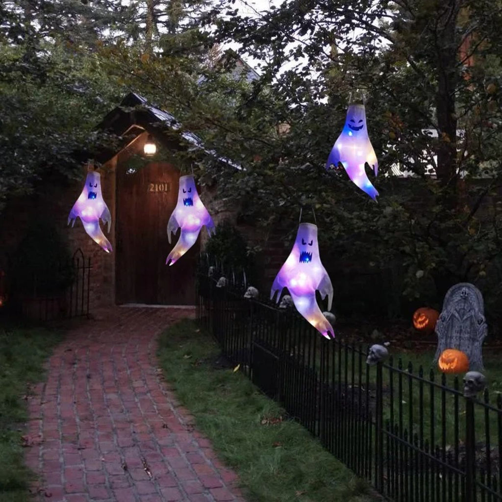 Flere tente halloween spøkelser hengende langs en hagesti med gresskar og gjerde
