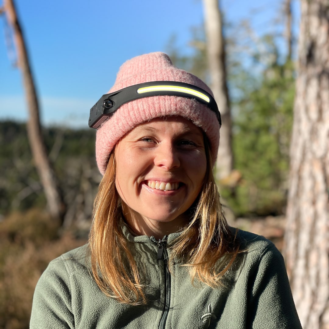 Kvinne med rosa lue og Vidsyn-hodelykten på pannen i skogen