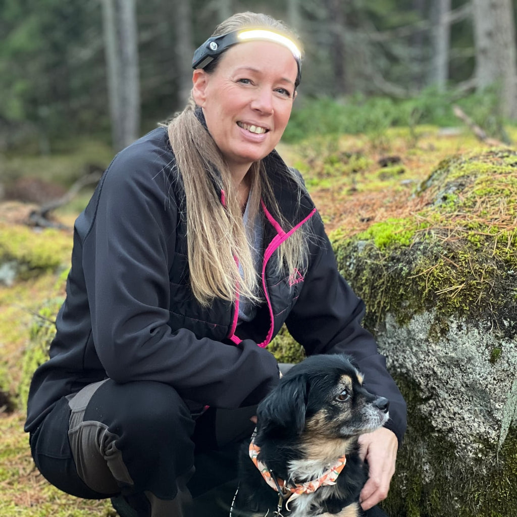Kvinne med hodelykten på tur i skogen sammen med hunden