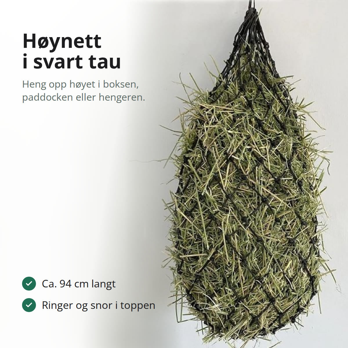 Svart høynett av knyttet tau, fylt med høy og hengt opp på en lys vegg