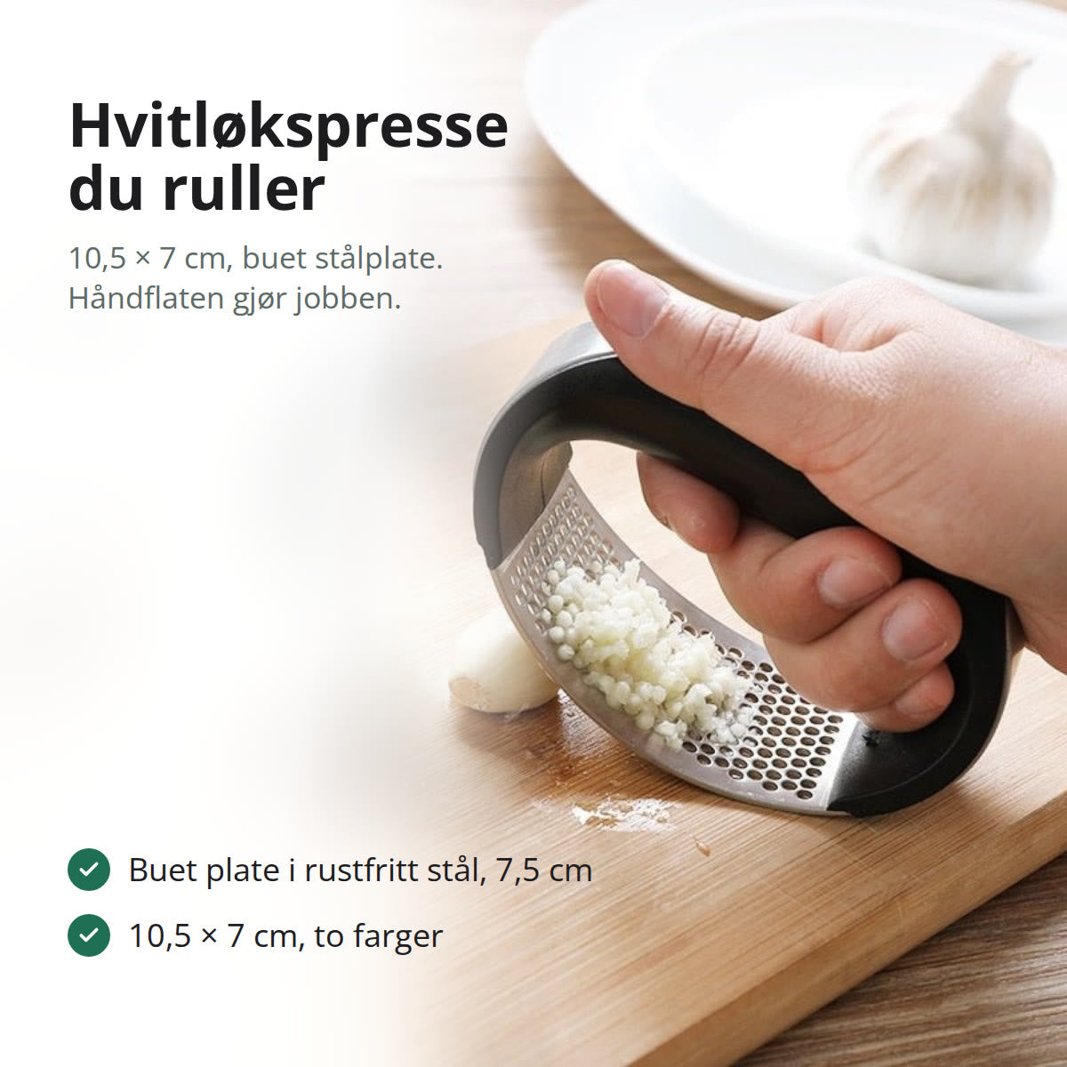 Hvitløkspresse i sort plast og rustfritt stål, liggende på en skjærefjøl med hvitløk
