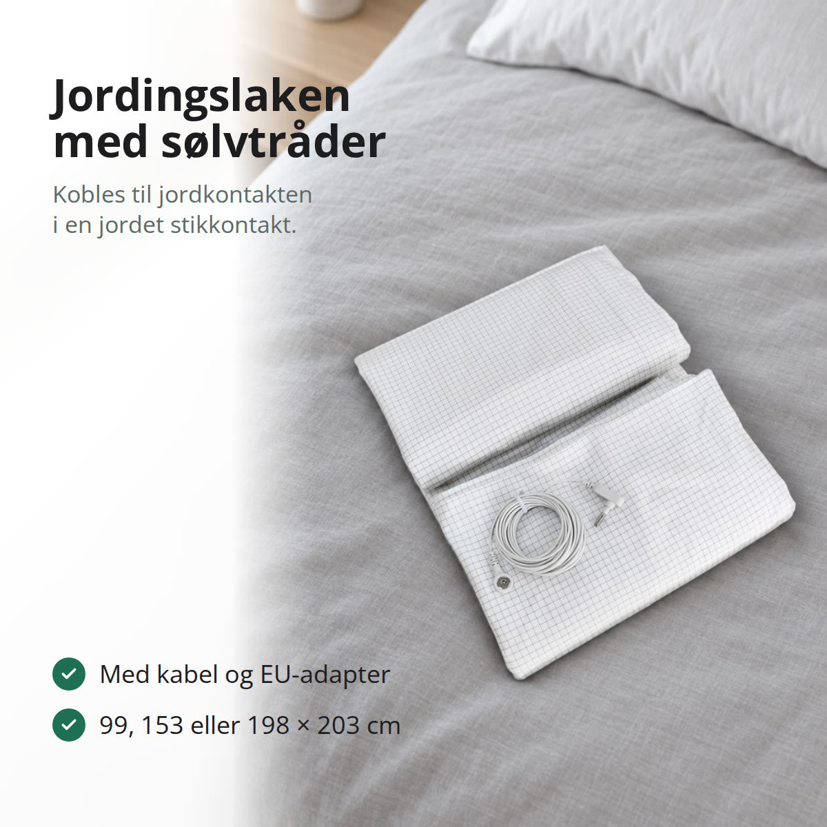 Jordingslaken i bomull med sølvtråder, brettet sammen med jordingskabelen på en seng med lys grå dyne i et lyst soverom