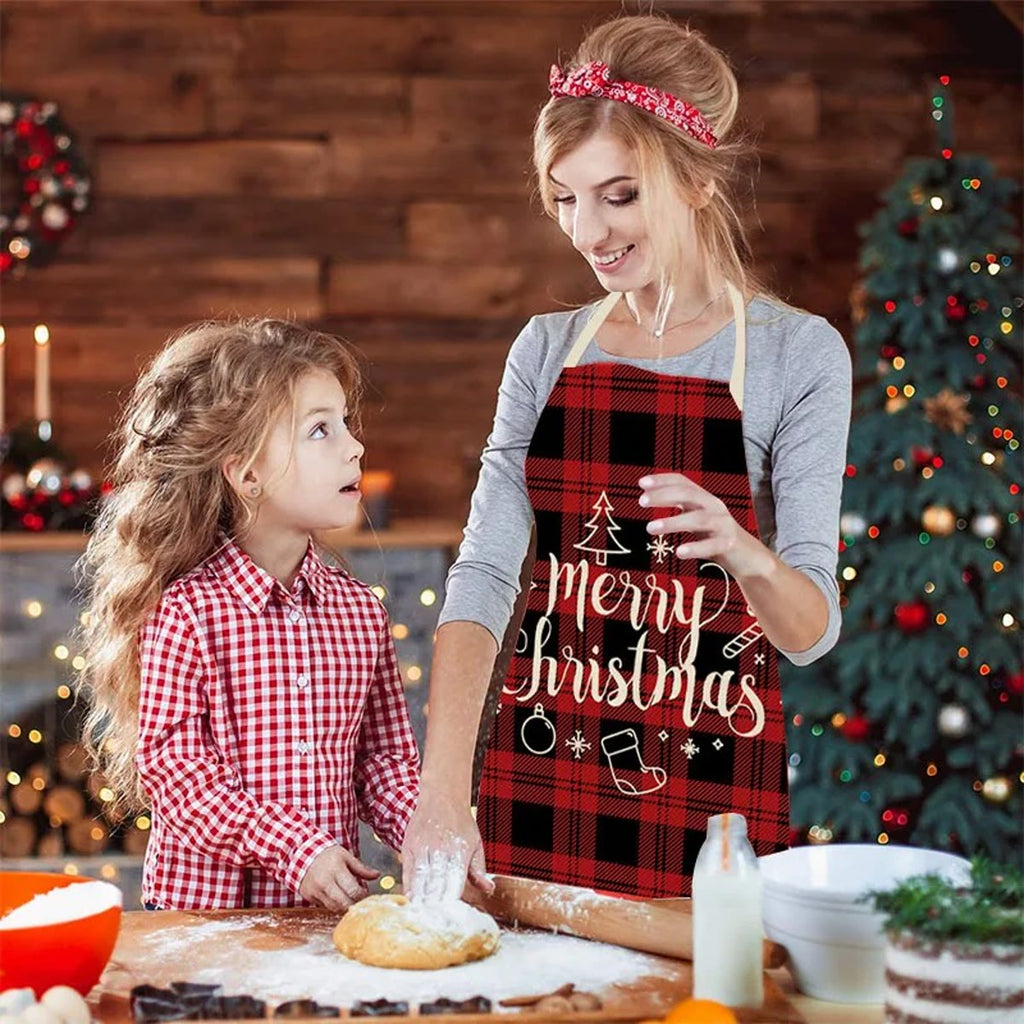 Mor og datter baker ved kjøkkenbordet; mor har på seg juleforkle i rød og svart rute med Merry Christmas