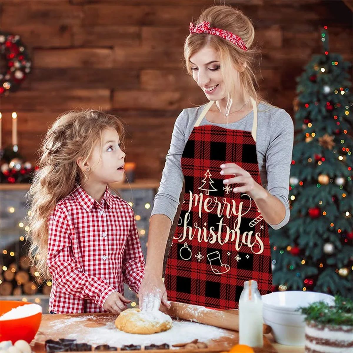 Mor og datter baker ved kjøkkenbordet; mor har på seg juleforkle i rød og svart rute med Merry Christmas