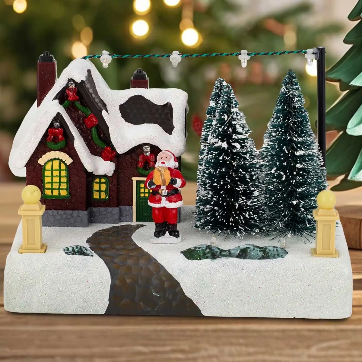 Julelandsbyen slukket i dagslys foran et juletre, huset med snøtak og nissen ved døren