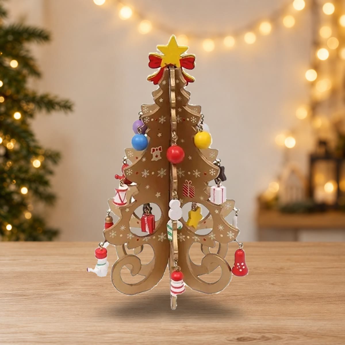 Gullfarget juletre i tre med små trepynt på et trebord foran julelys