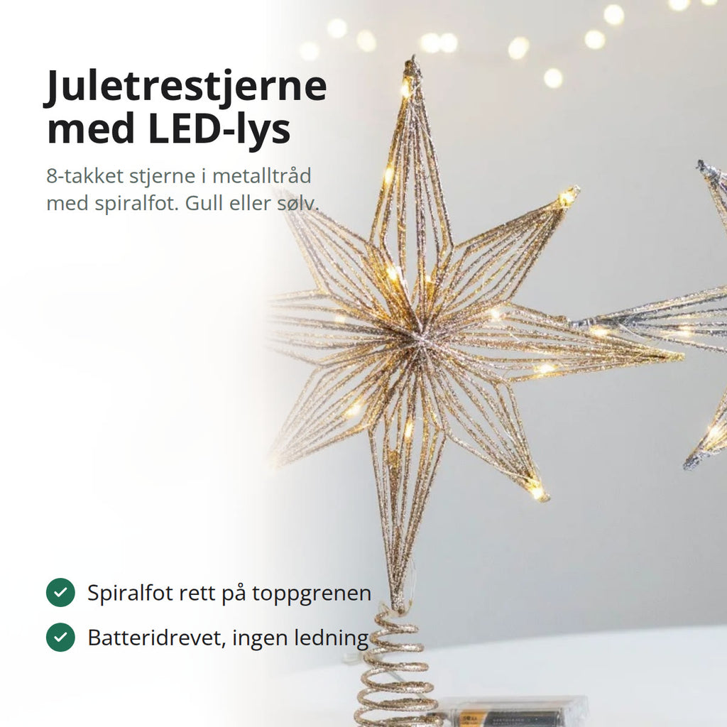 Juletrestjerne i gullfarget metalltråd med LED-lys og spiralfot, stående på et bord ved siden av julekuler