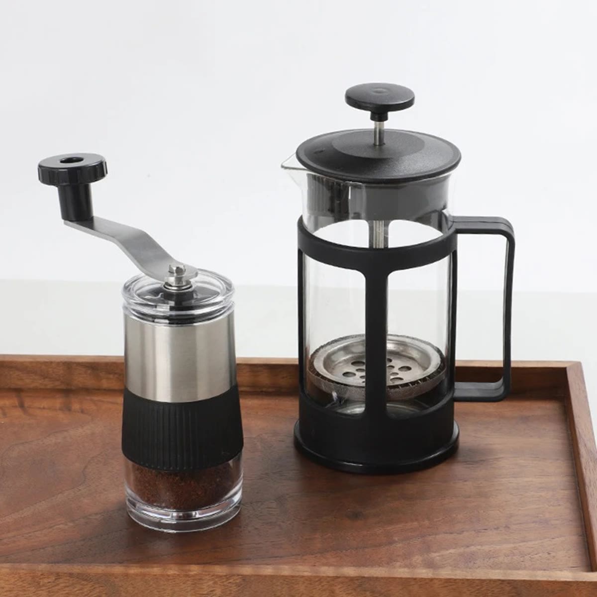 Manuell kaffekvern med malt kaffe ved siden av en presskanne på et trebrett