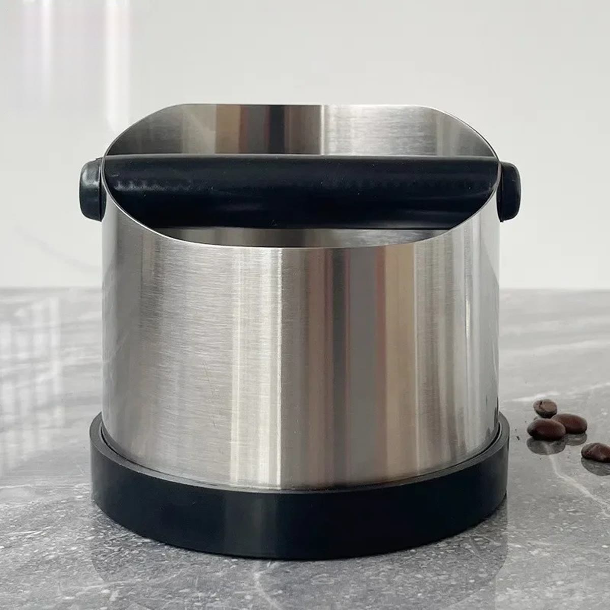 Knock boxen sett forfra på en grå marmorbenk, med stangen på tvers av åpningen og noen kaffebønner ved siden av