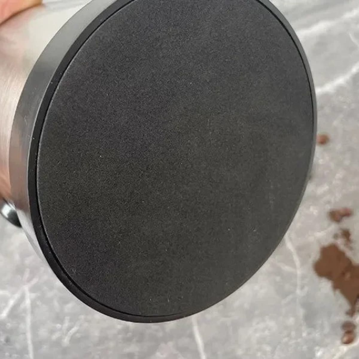 Undersiden av knock boxen med den sklisikre bunnen, holdt i en hånd over en marmorbenk med litt kaffegrut