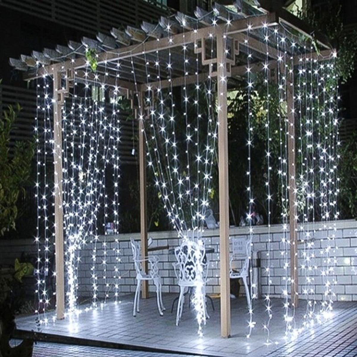 Lysgardin hengt opp i en hvit pergola på en terrasse om kvelden