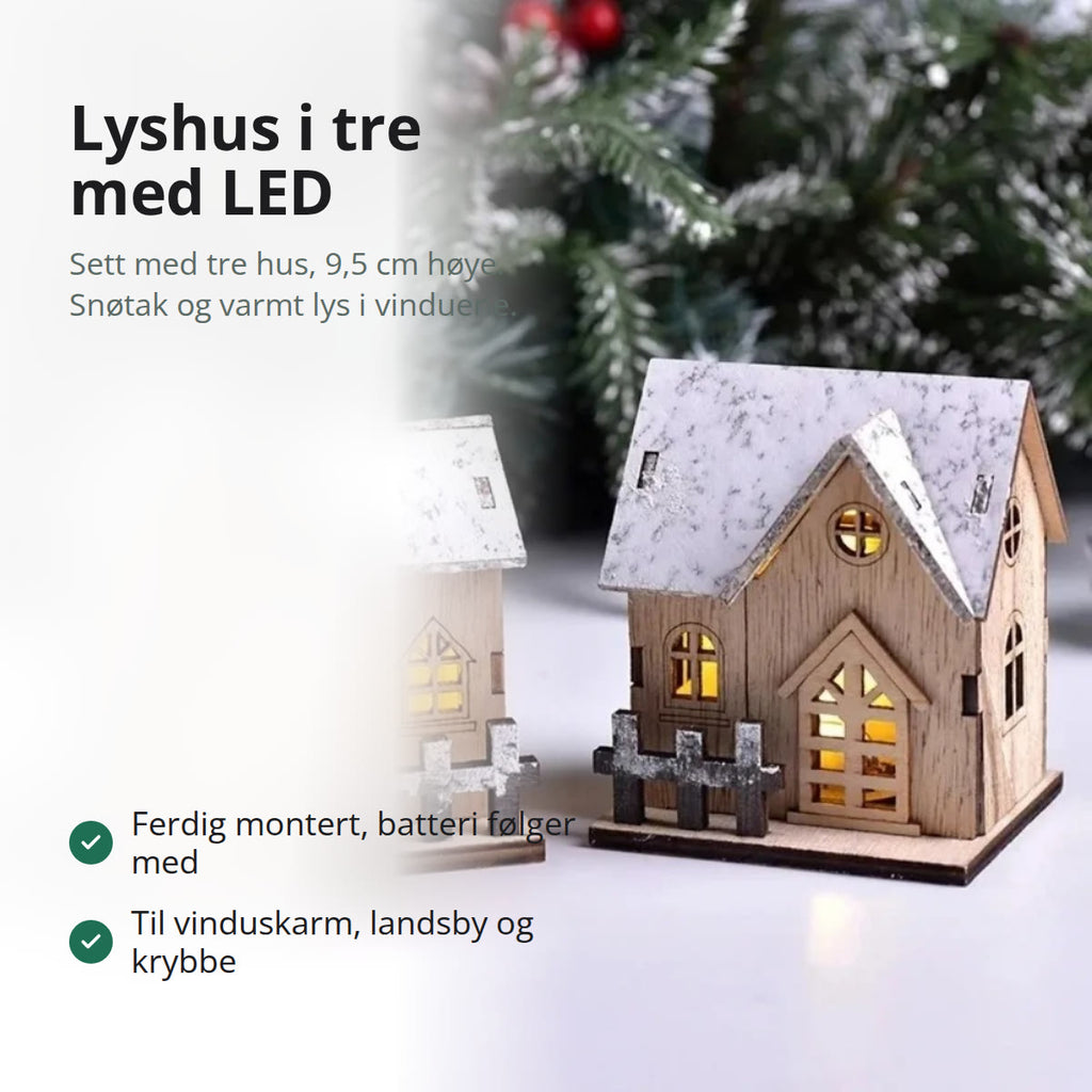 Tre små lyshus i lyst tre med hvitt snøtak og varmt LED-lys i vinduene, på et bord med grankvister