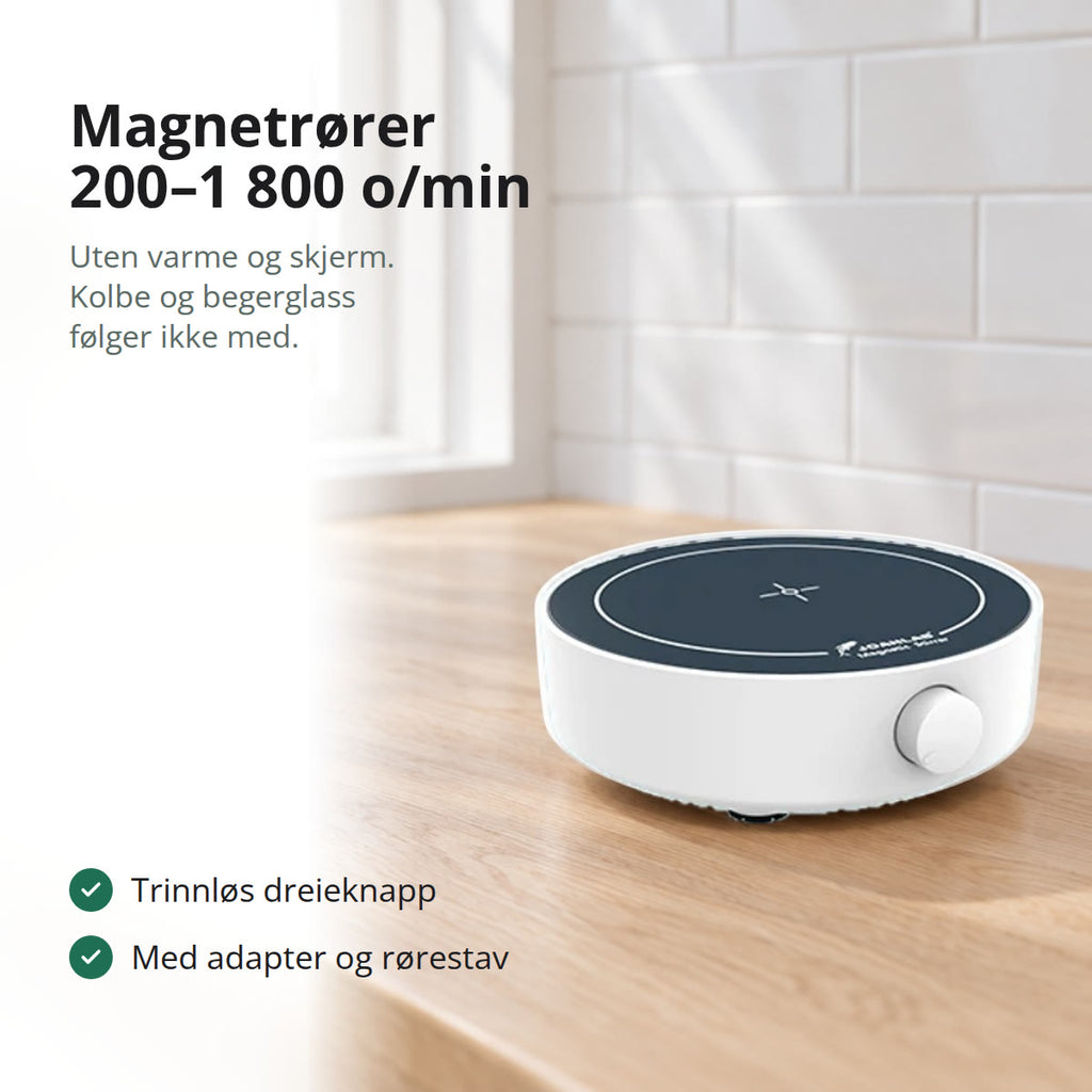 Hvit magnetrører med mørk plate og dreieknapp på en benkeplate i lys eik, med hvite fliser og vindu mot fjell og fjord