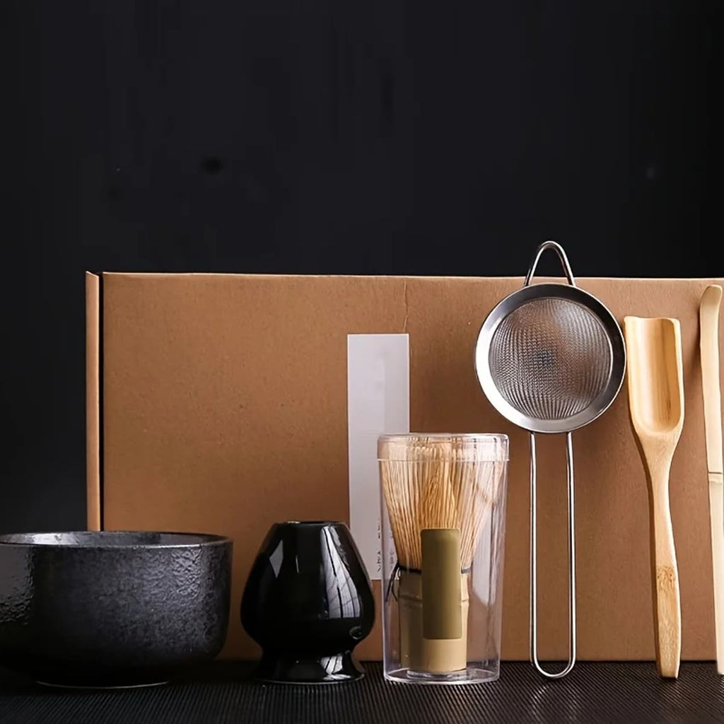 Matcha-sett i svart med bolle, vispholder, bambusvisp, sil og bambusskjeer foran gaveesken