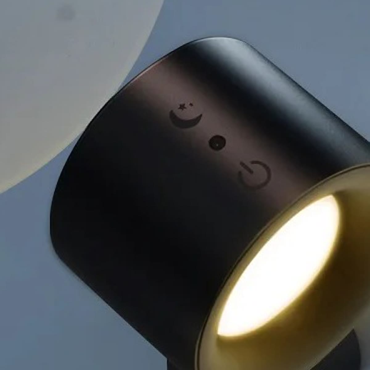 Svart vegglampe med varmt lys på en blågrå vegg