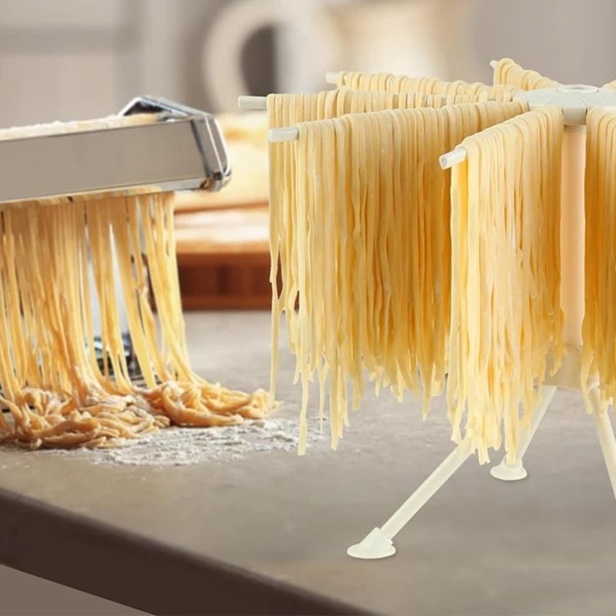 Pastastativ med fersk spagetti ved siden av en pastamaskin på kjøkkenbenken