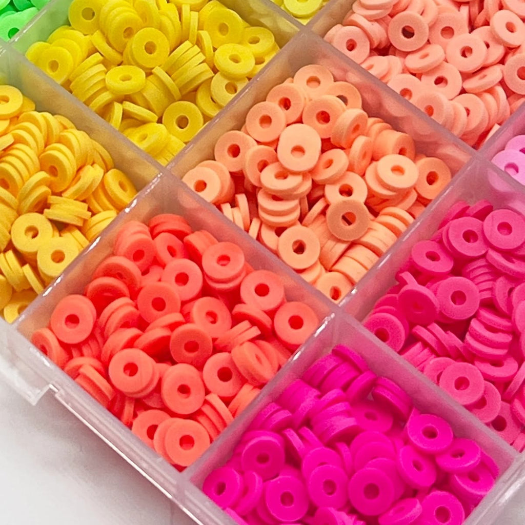 Nærbilde av flate leirperler i gult, fersken, korall og sterk rosa i hvert sitt rom, hullet i midten synlig