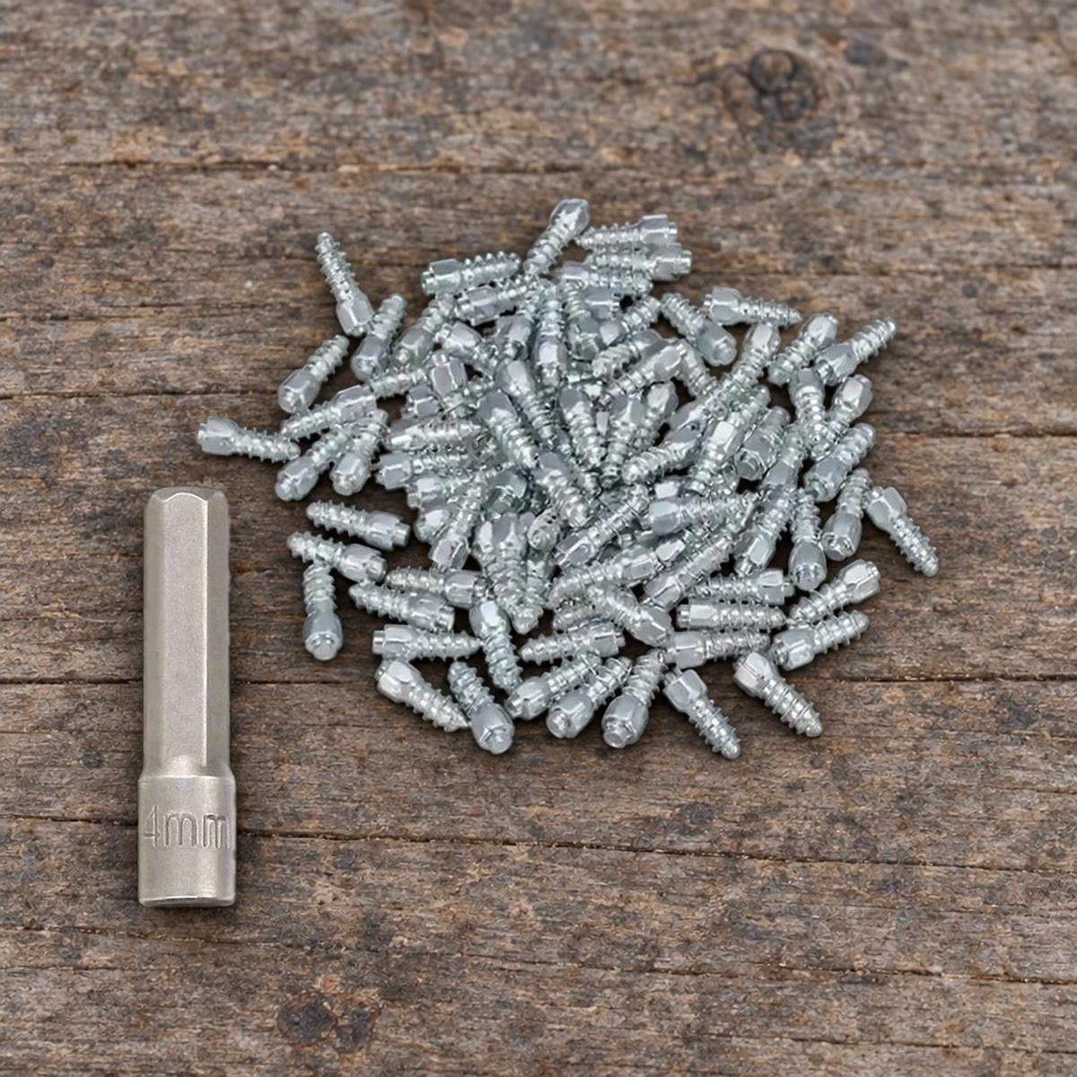Haugen med 50 skrupigger og monteringsbiten merket 4mm, på en arbeidsbenk i grått treverk