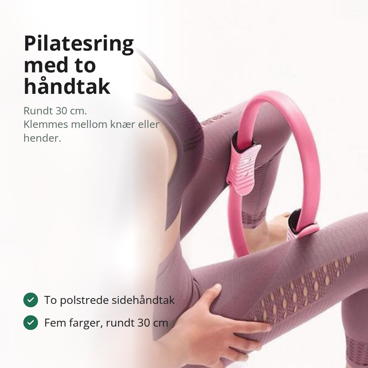 Pilatesring i sort med to polstrede sidehåndtak, liggende på en grå treningsmatte