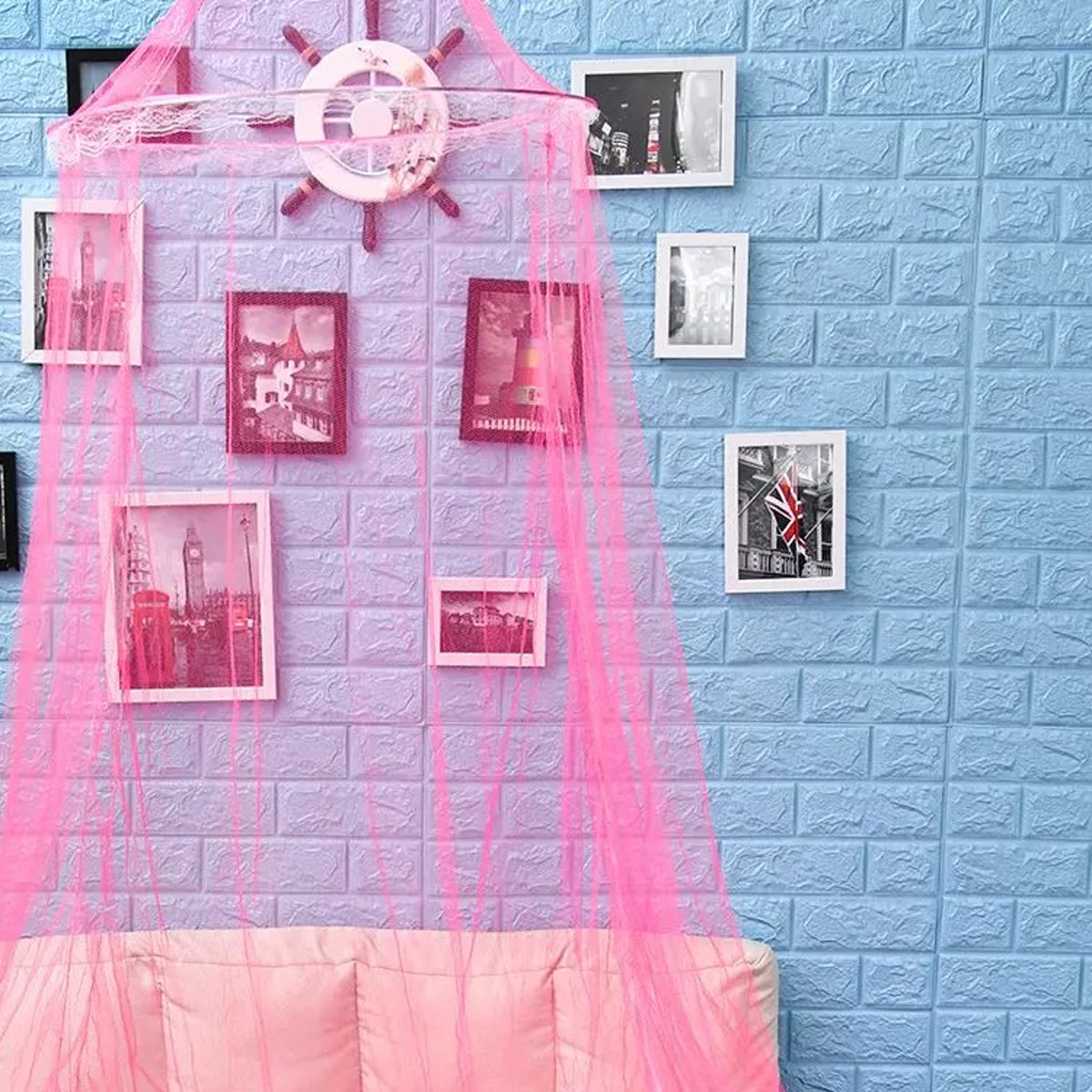 Toppen av den rosa sengehimmelen med ringen og den hvite blondekanten foran en vegg med bilder