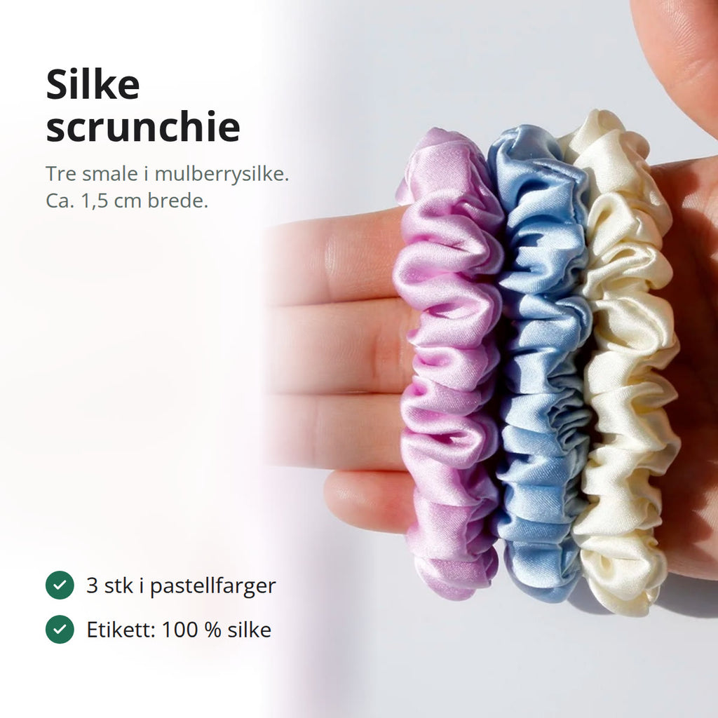 Tre smale silke scrunchies i rosa-lilla, lyseblått og krem i en åpen hånd