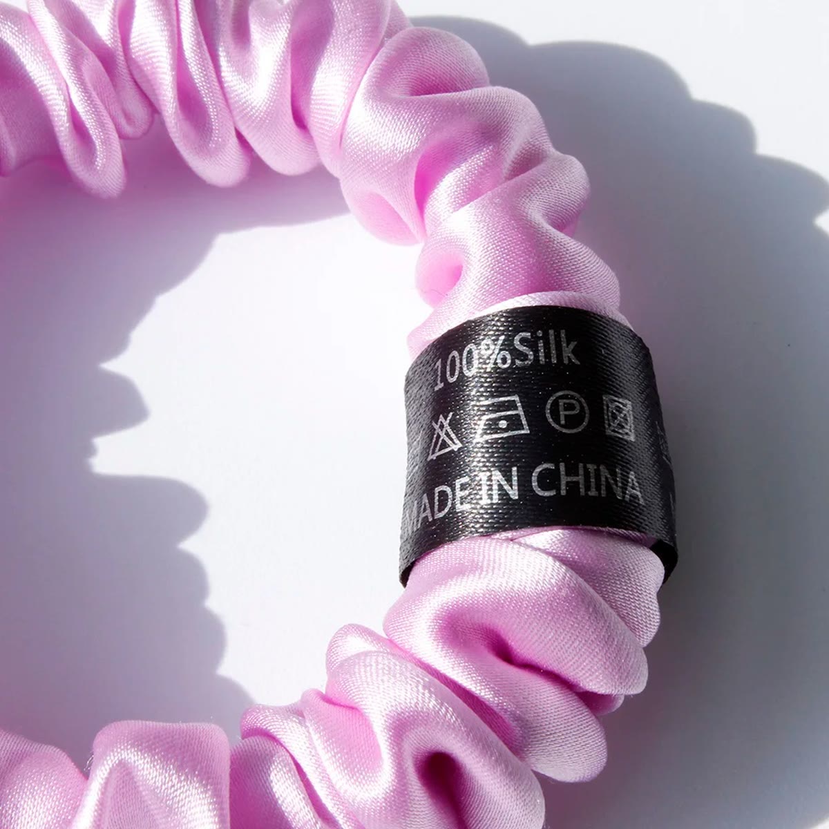 Nærbilde av etiketten 100% Silk på en rosa-lilla silke scrunchie