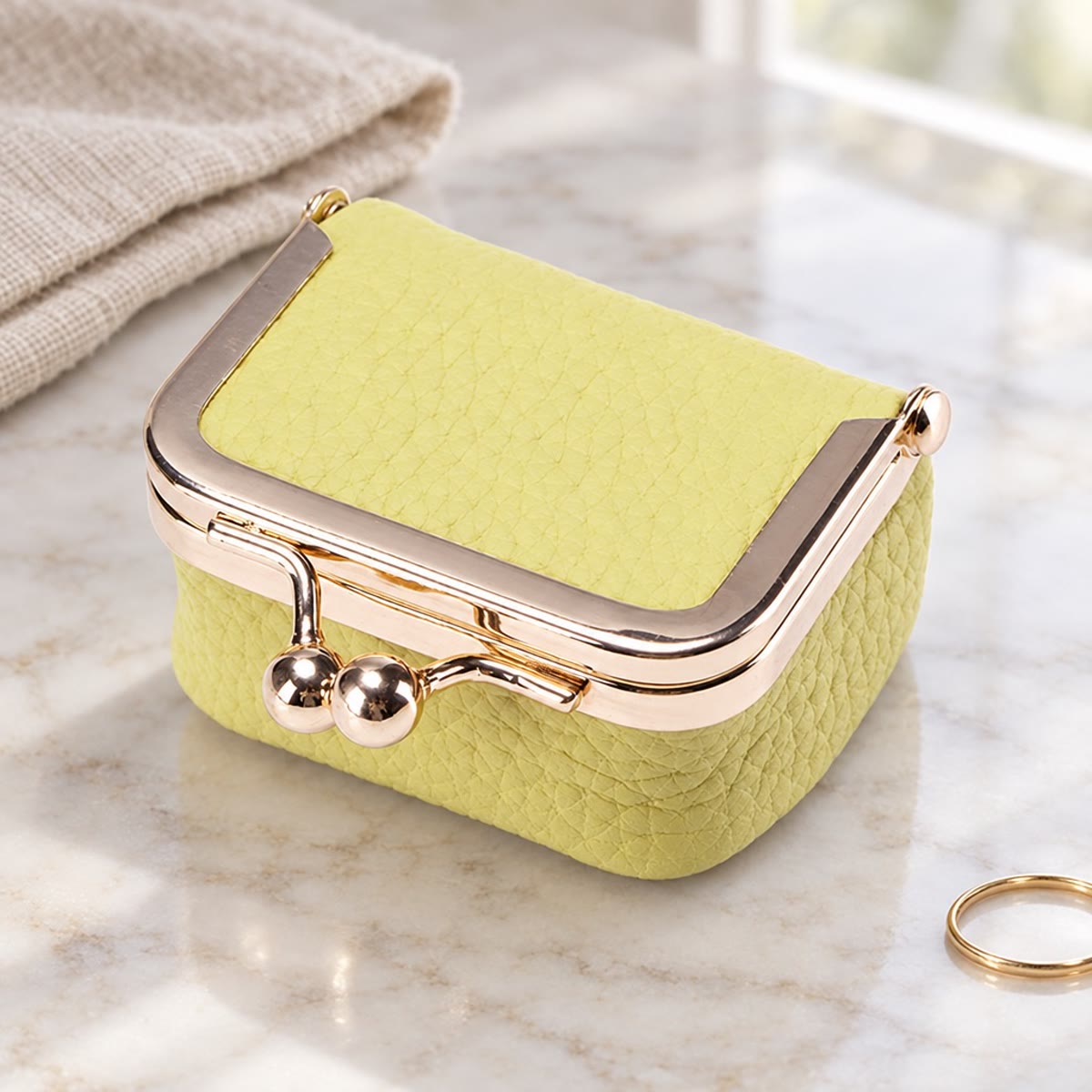 Gult smykkeskrin i skinn med gullås ved siden av en tynn ring